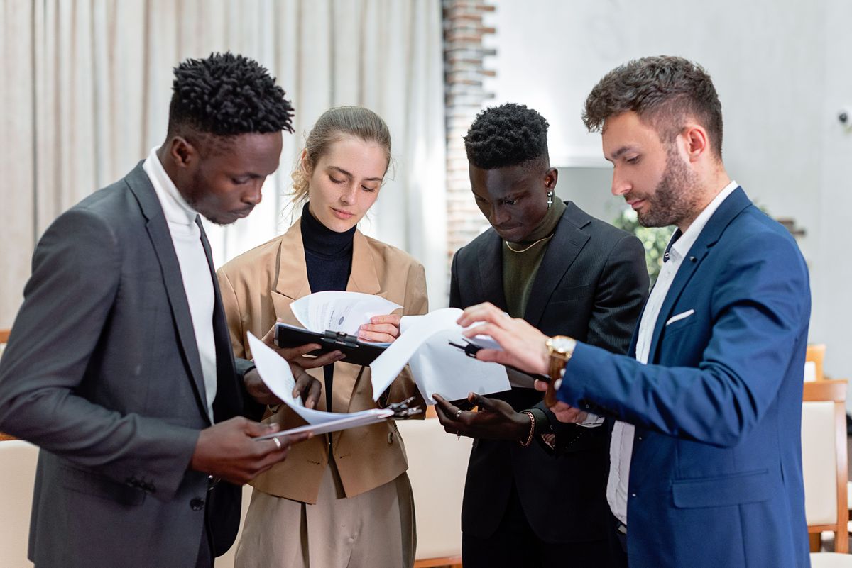 Four people in business attire reviewing printed financial documents together